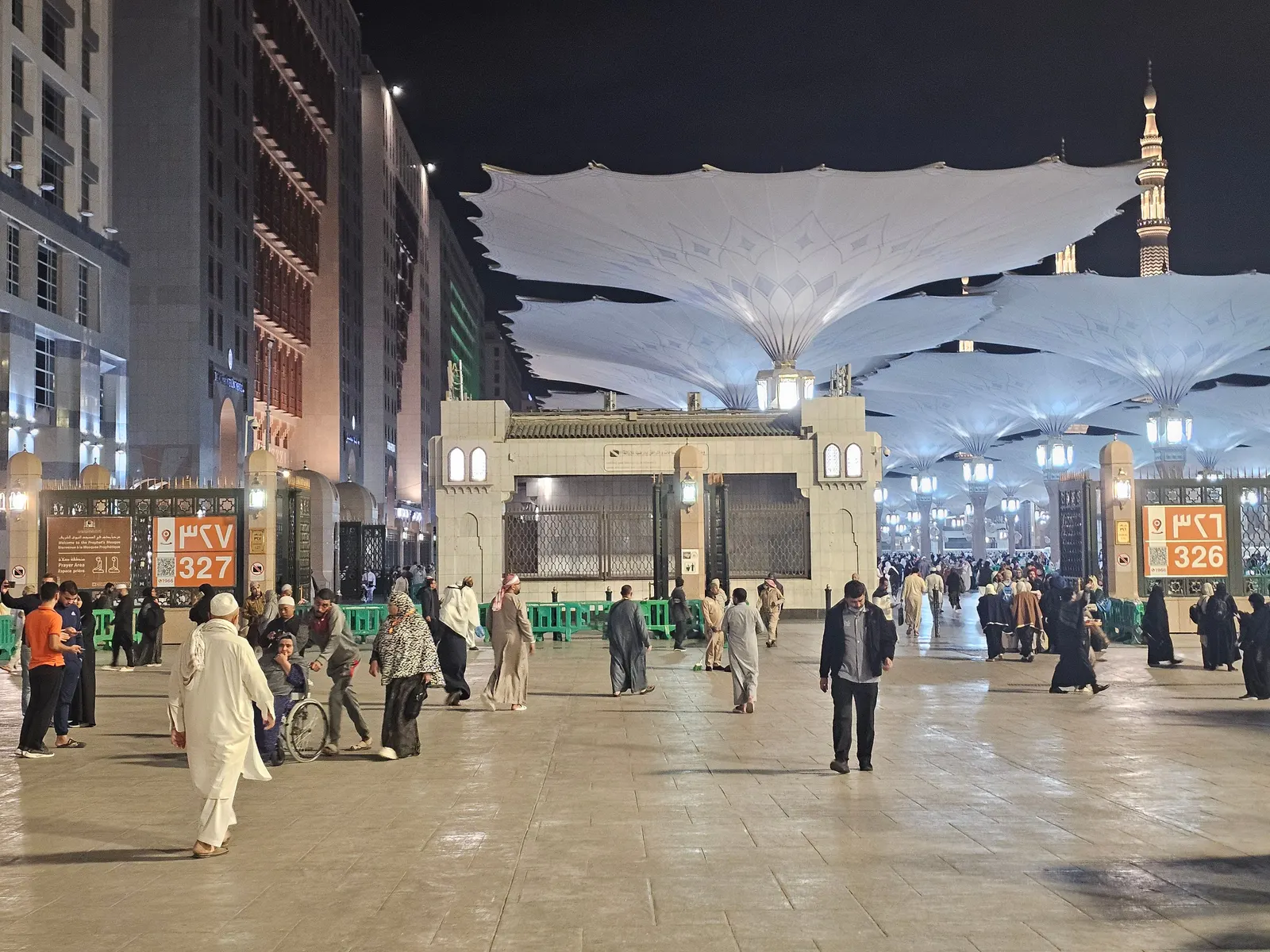 The illuminated courtyard of Masjid an-Nabawi at night, with worshippers at a distance