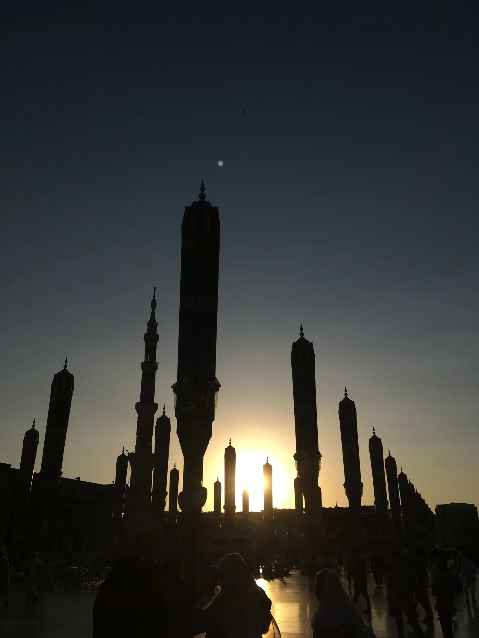 Silhouettes of folded umbrellas and a minaret of Masjid an-Nabawi against the sunset sky